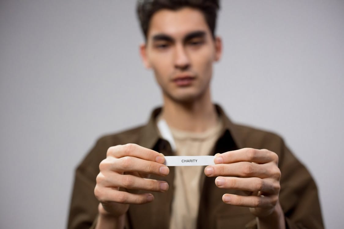 Free A man holds a note reading 'charity,' with the focus on his hands, expressing a charitable theme. Stock Photo