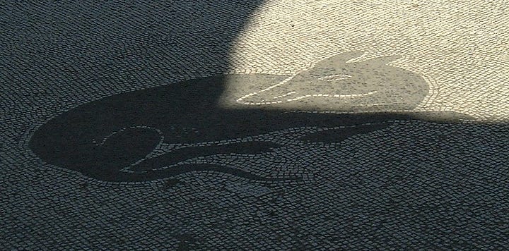 One mosaic of a dog lying down: the other a real dog lying down