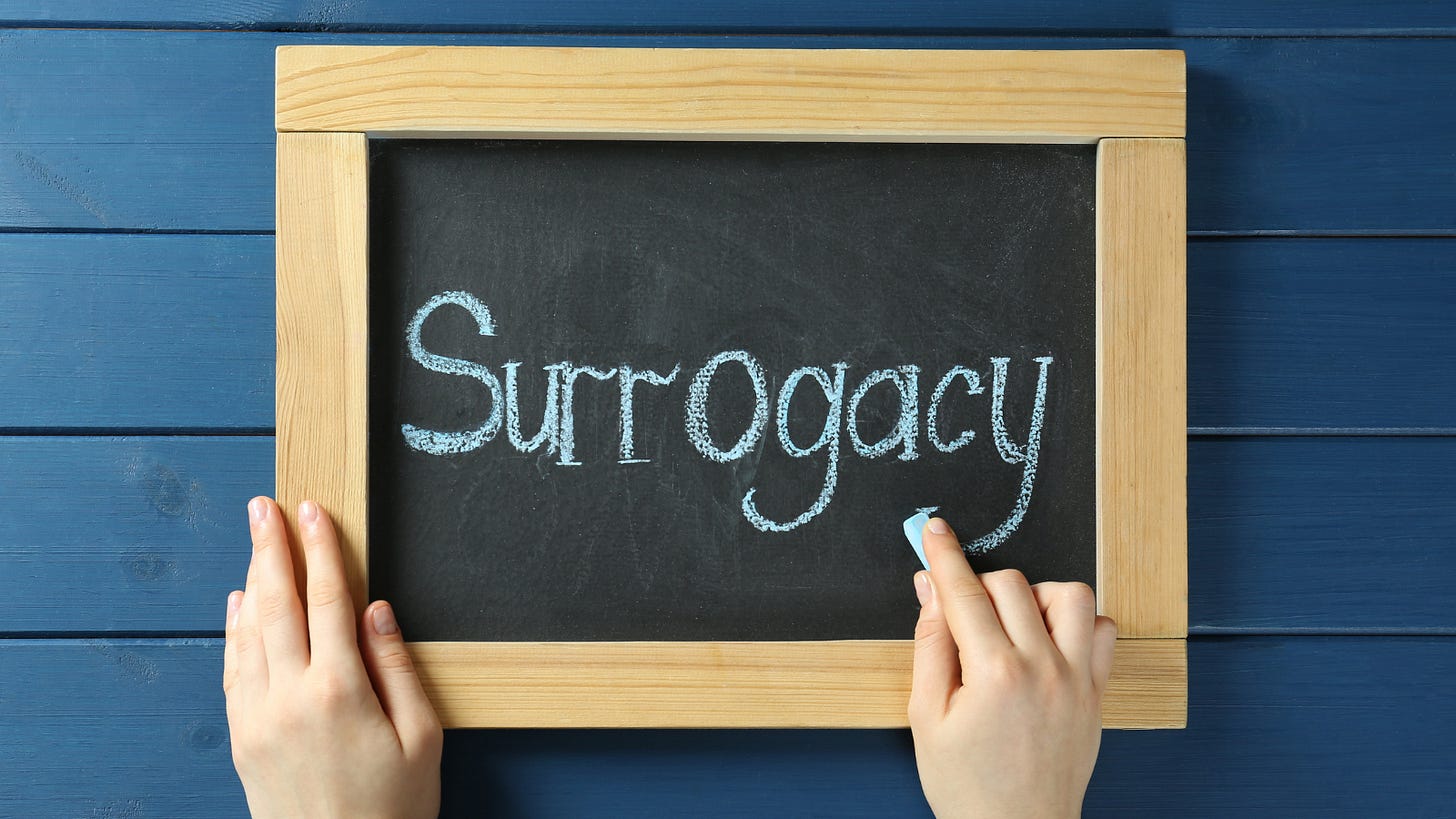 A pair of hands holding a small chalkboard with the word Surrogacy written in white chalk.
