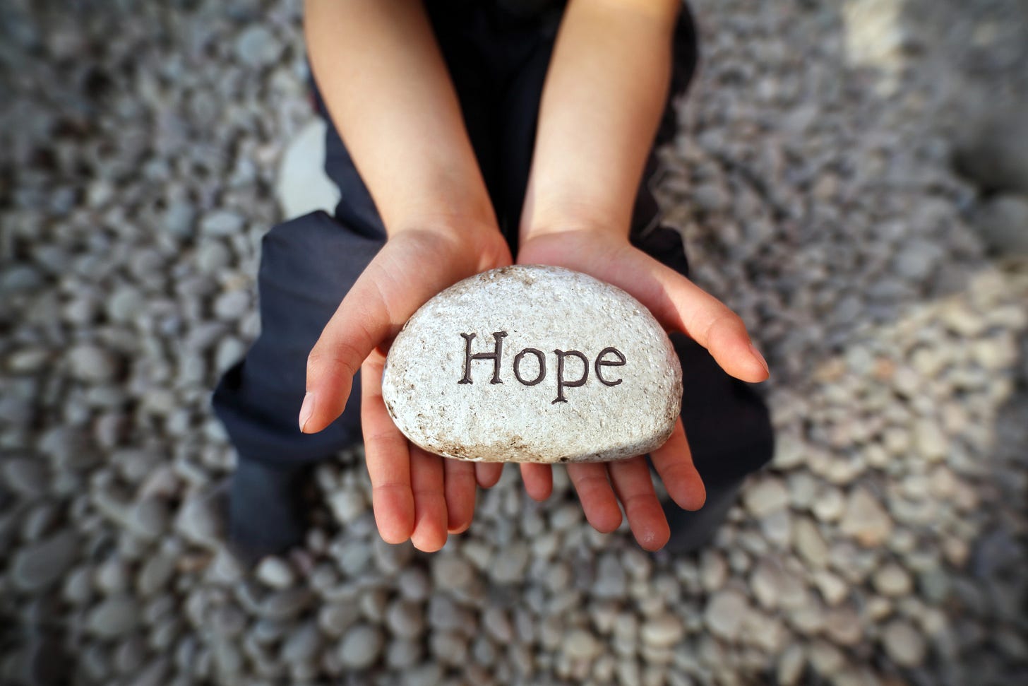 Two hands with a rock in them with the word "HOPE" carved into it
