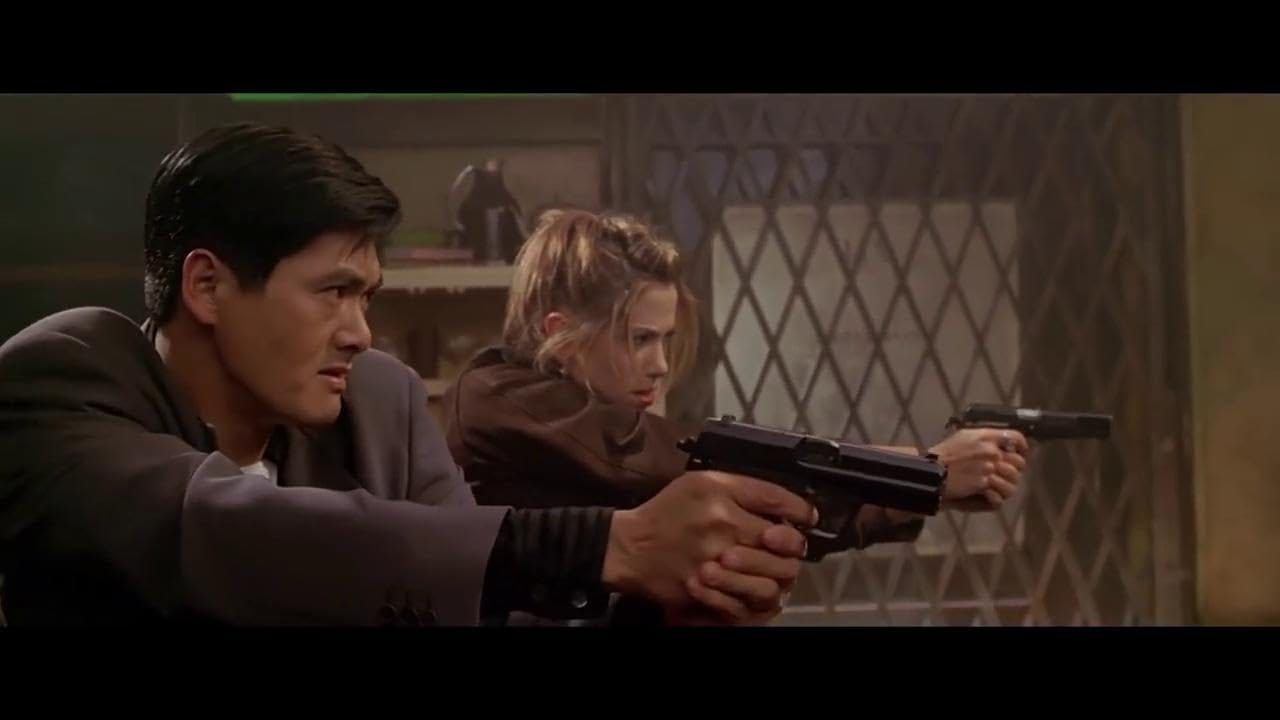 Chow Yun-Fat and Mira Sorvino side by side, aiming their pistols in sync during an action sequence from The Replacement Killers.