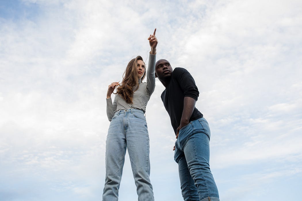 A woman gives a man directions against a background of light blue sky with clouds. A woman gives a man directions against a background of light blue sky with clouds.