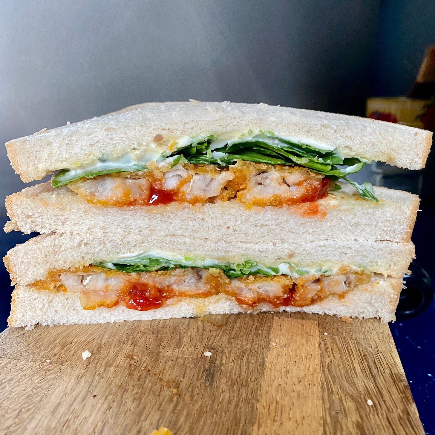Fish finger sandwich on white bread, with salad, ketchup, served on a wooden board