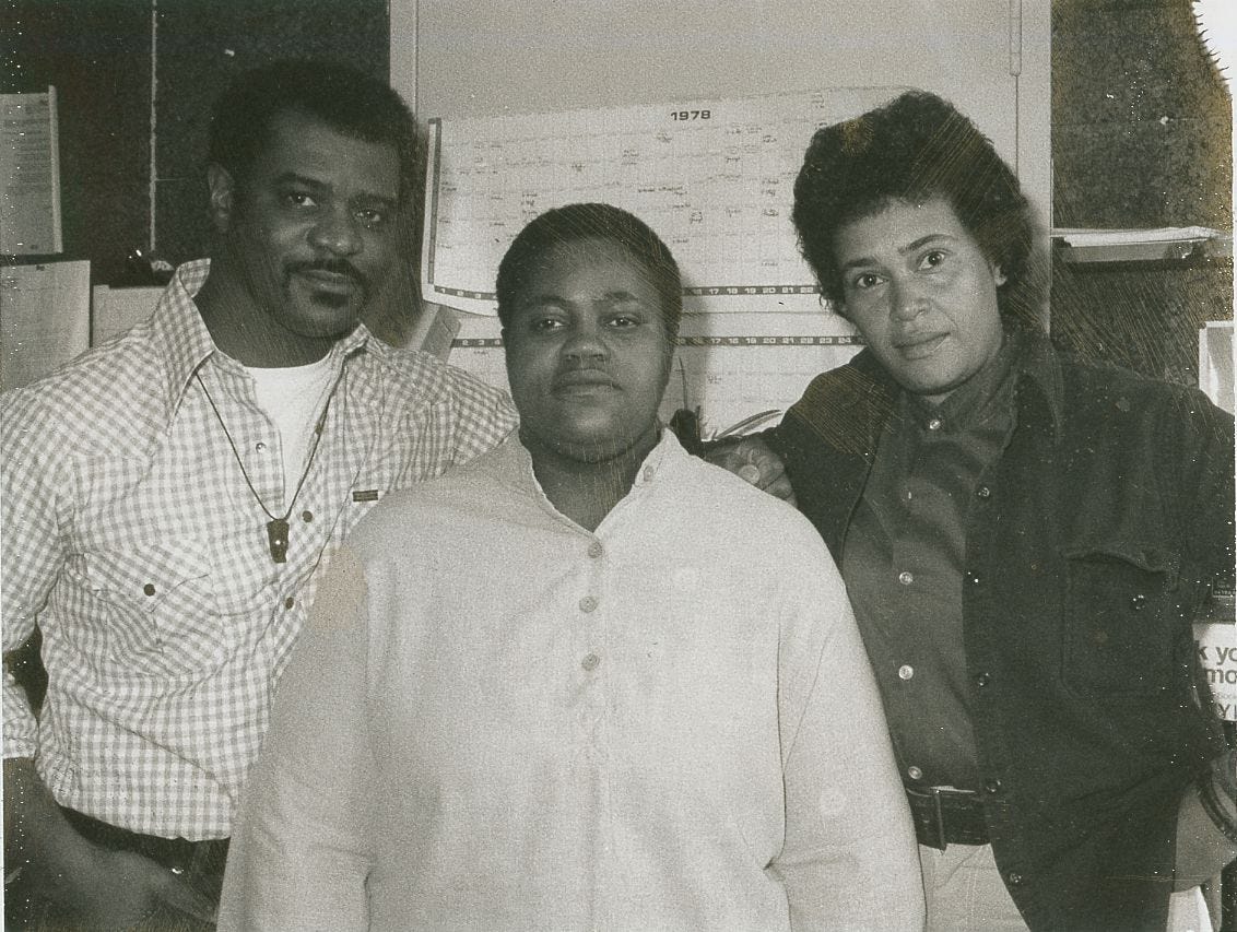 Black-and-white photograph of three members of the National Gay Task Force Third World Caucus standing together indoors in front of a 1978 calendar. From left to right: A. Billy S. Jones, Sean Reynolds, and Pat Norman. Taken in February 1979. Courtesy of Cornell University Library.