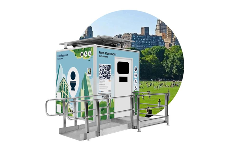 a real life mockup of the public restroom unit in front of a open field with people