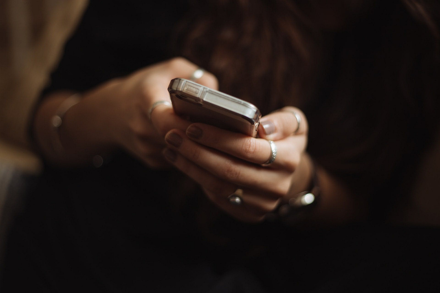 A close-up shot of two hands with rings and painted nails clutching a phone
