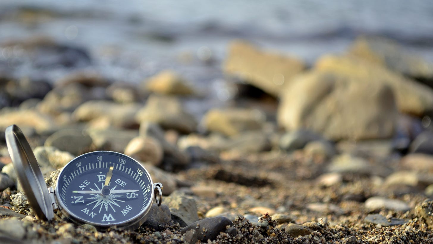 A silver compass resting among pebbles on a shoreline, symbolizing direction, clarity, and reorientation after change. A silver compass resting among pebbles on a shoreline, symbolizing direction, clarity, and reorientation after change.