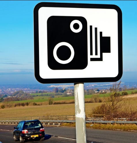 A sign for a speed camera on the side of a road.