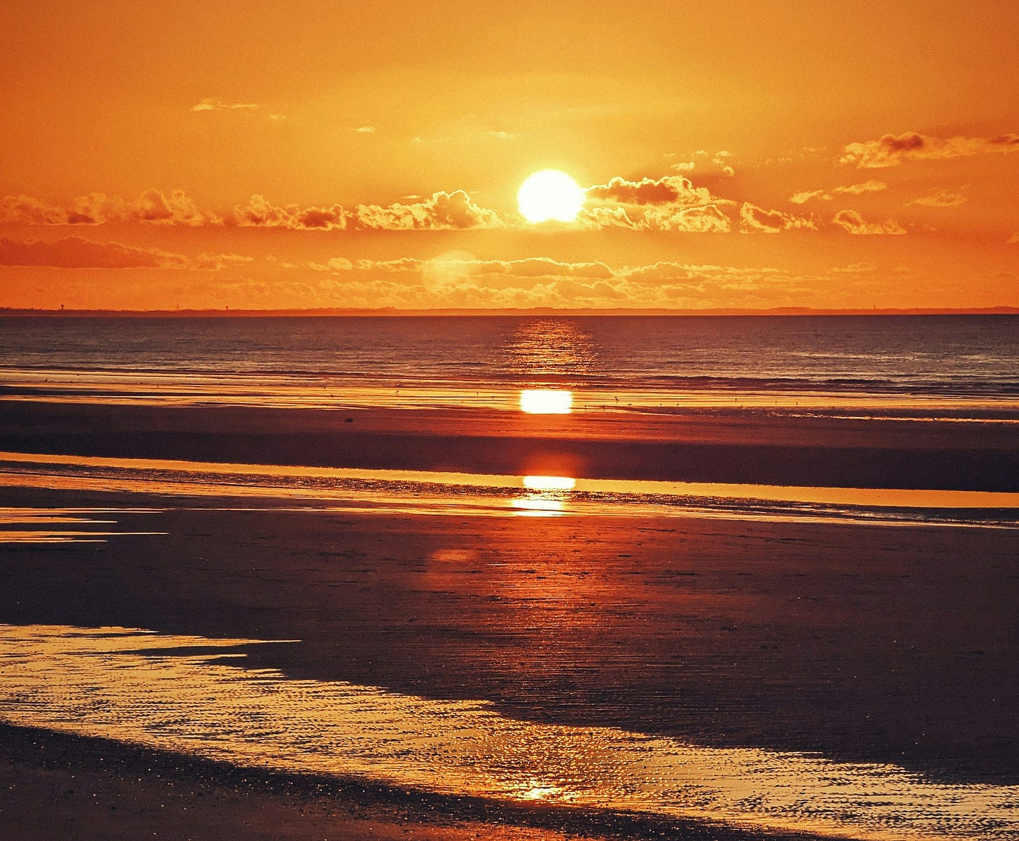 The sun is setting over the water on the beach