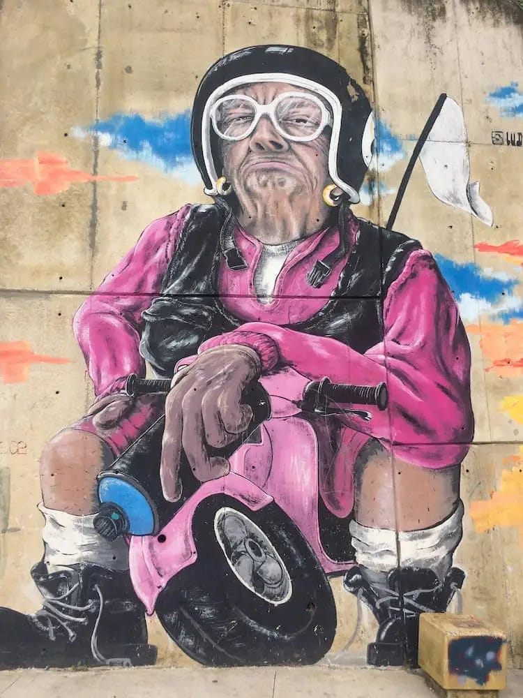 Street art - a man dressed in purple and wearing a crash helmet sits on a small bike