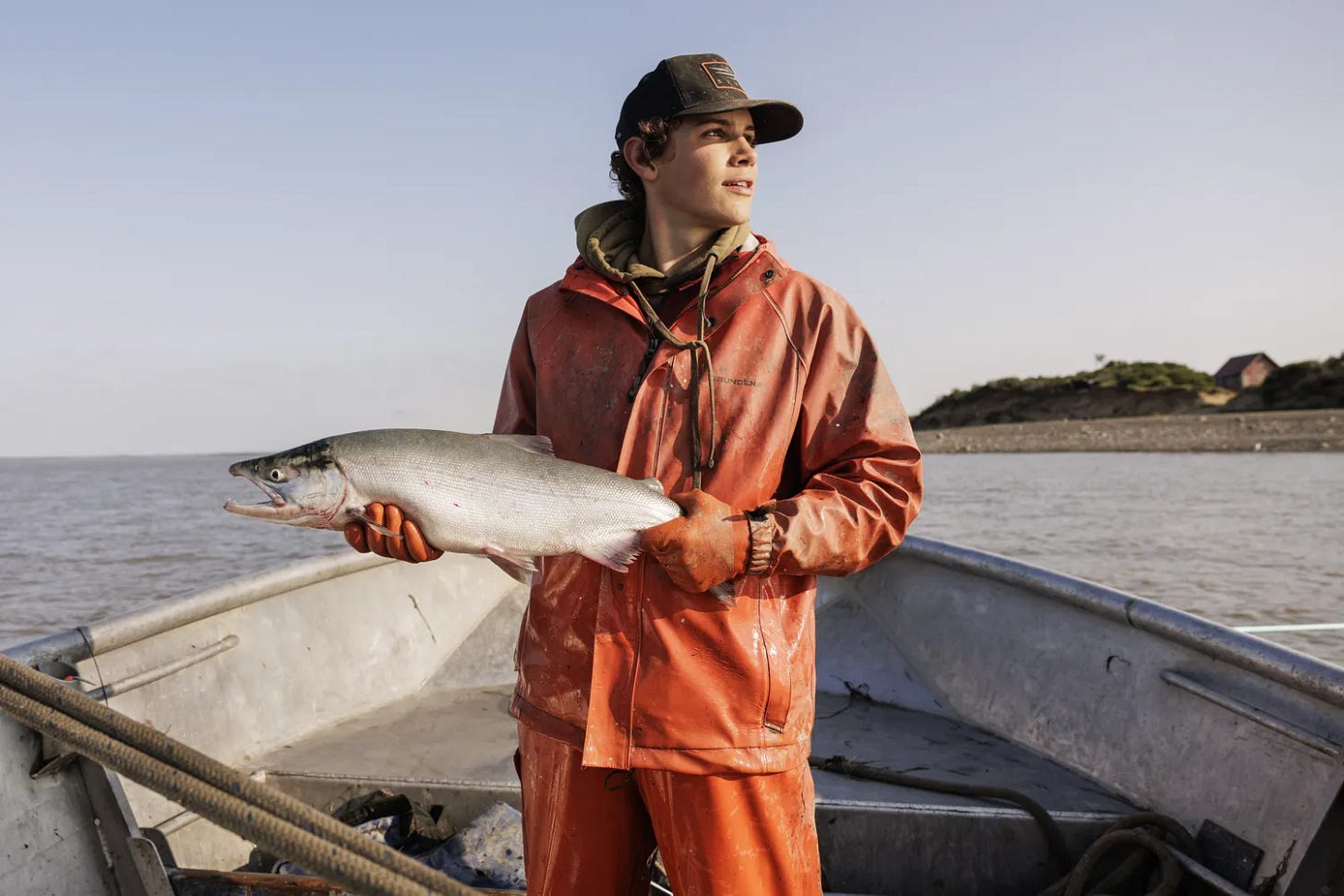 A person aboard a boat holding a fish near a body of water A person aboard a boat holding a fish near a body of water