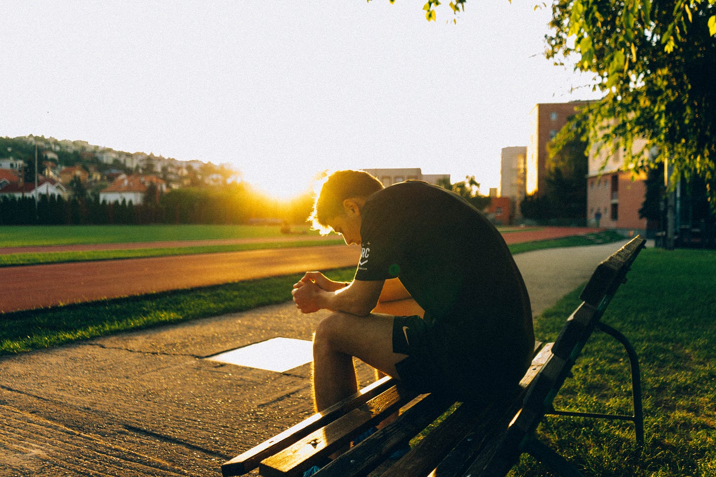Photo of a person sitting on a bench. They are hunched over, maybe sad or thoughtful. Time of day is sunrise or sunset. Photo of a person sitting on a bench. They are hunched over, maybe sad or thoughtful. Time of day is sunrise or sunset.
