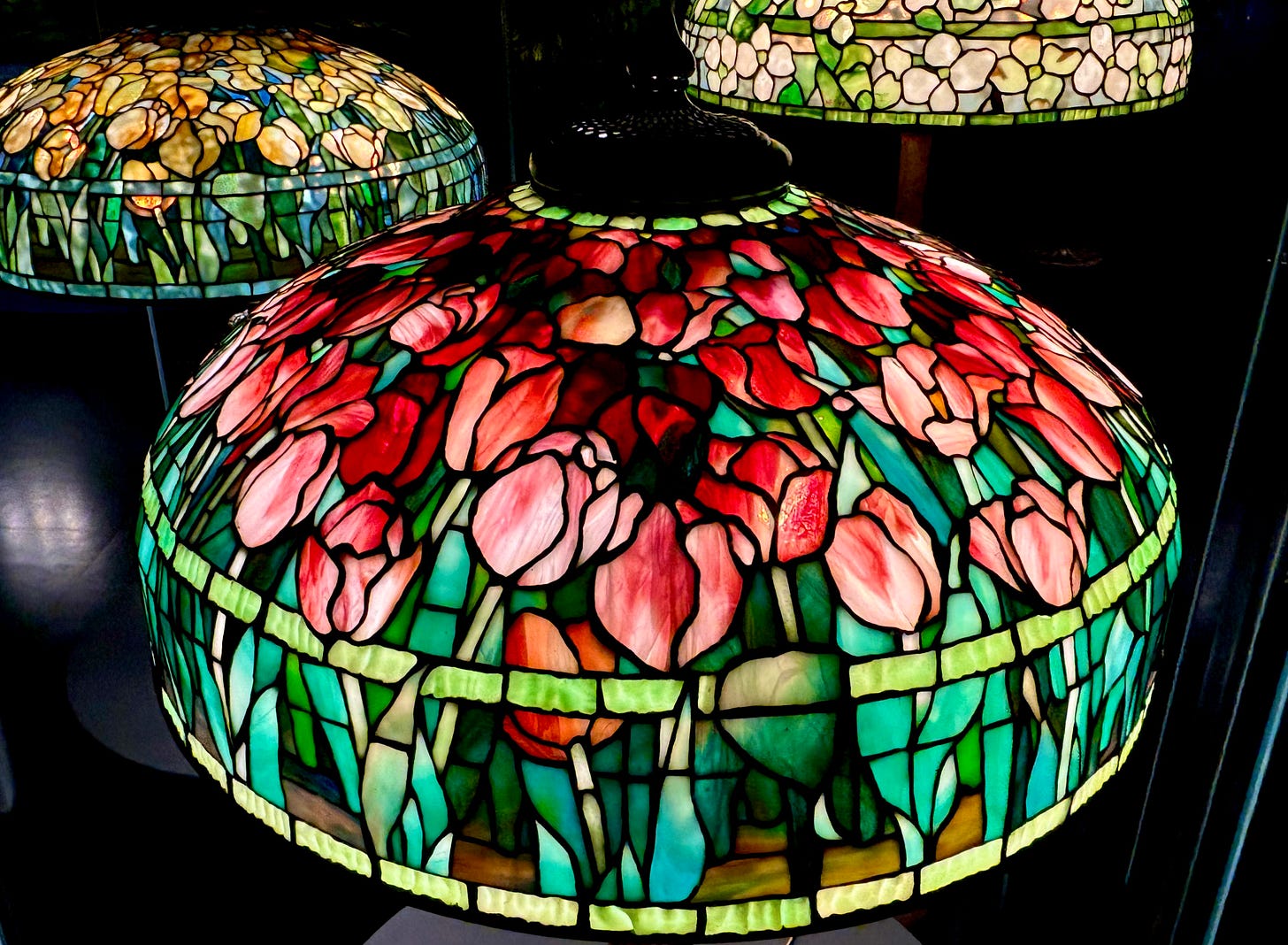 A closer and slightly higher view of the red tulip shade. Behind it is a shade of yellow tulips and to the right is a pretty white flower against green bands.