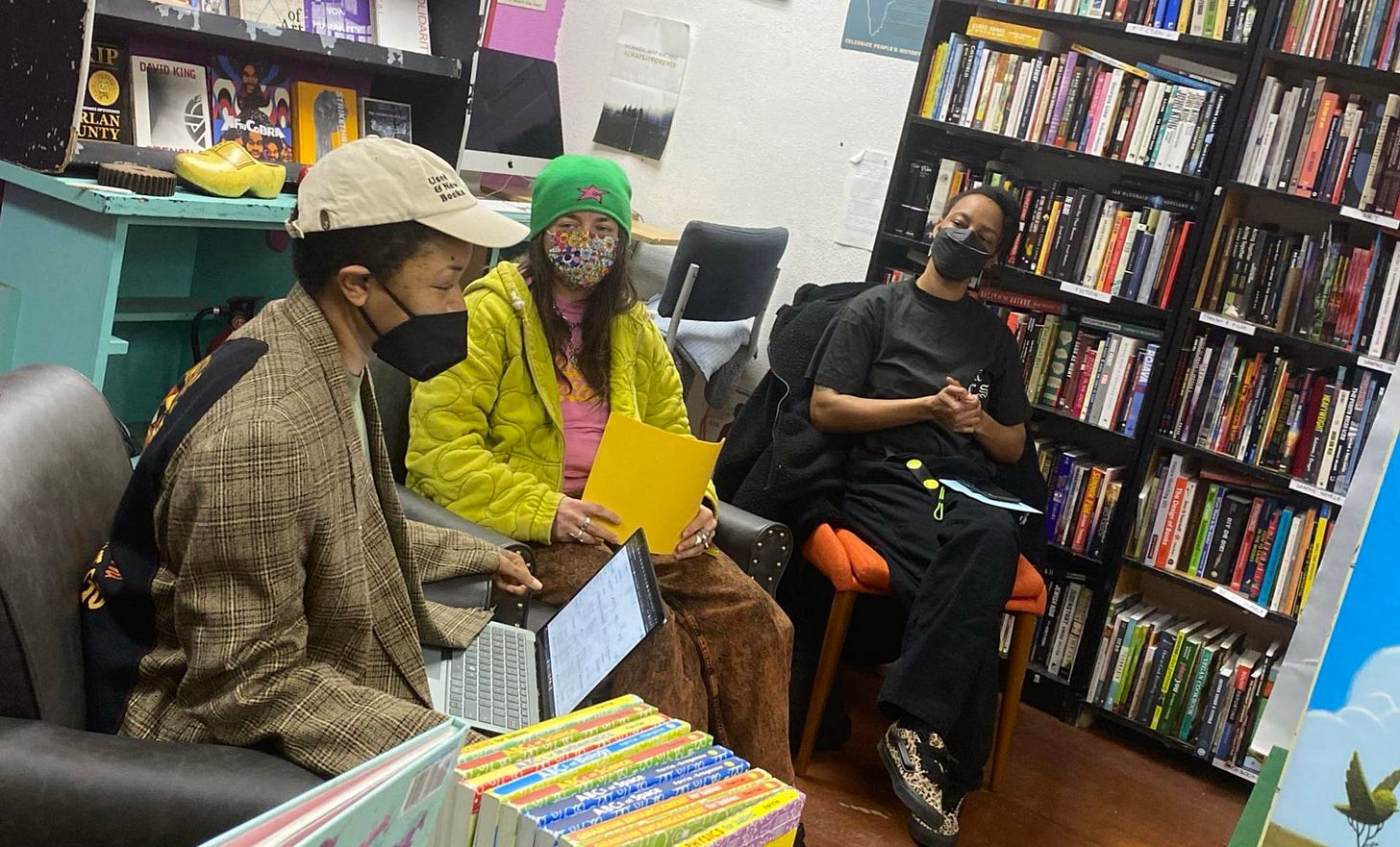 three people face an audience in chairs at a bookstore reading