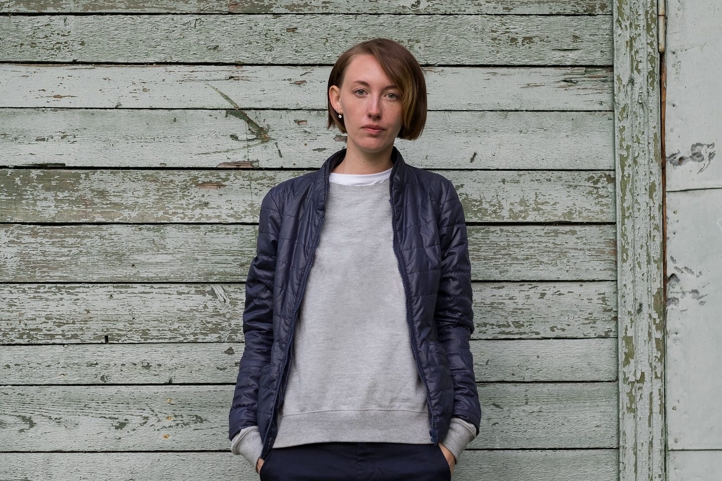 A woman with short hair stands against a faded wood-panel wall. A woman with short hair stands against a faded wood-panel wall.