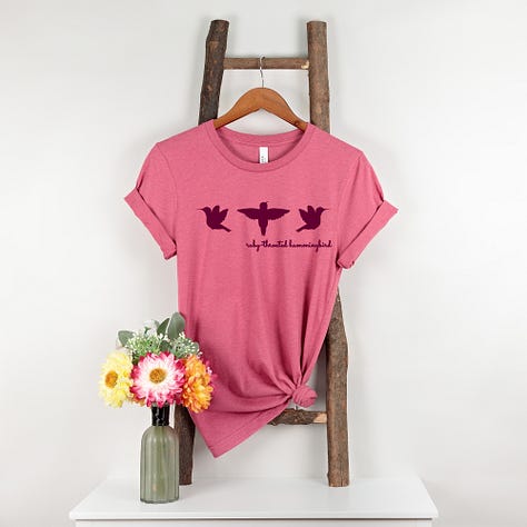 A gallery of three images shows Nature Moments Gear t-shirts in bright colors, featuring the Hummingbird Silhouettes design.