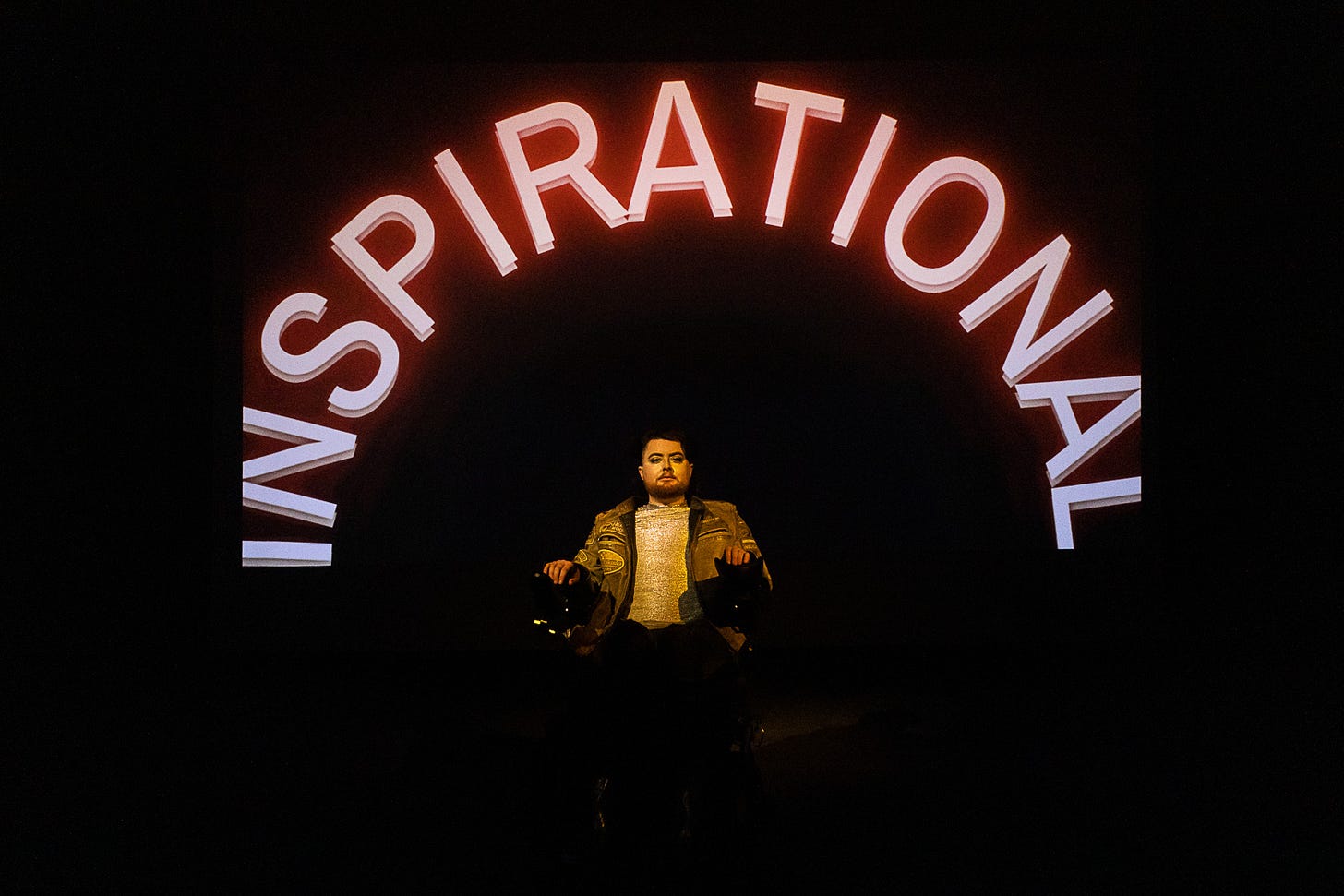 Jamie, a white electric wheelchair user sits against a black backdrop, the word "INSPIRATIONAL" arching around him