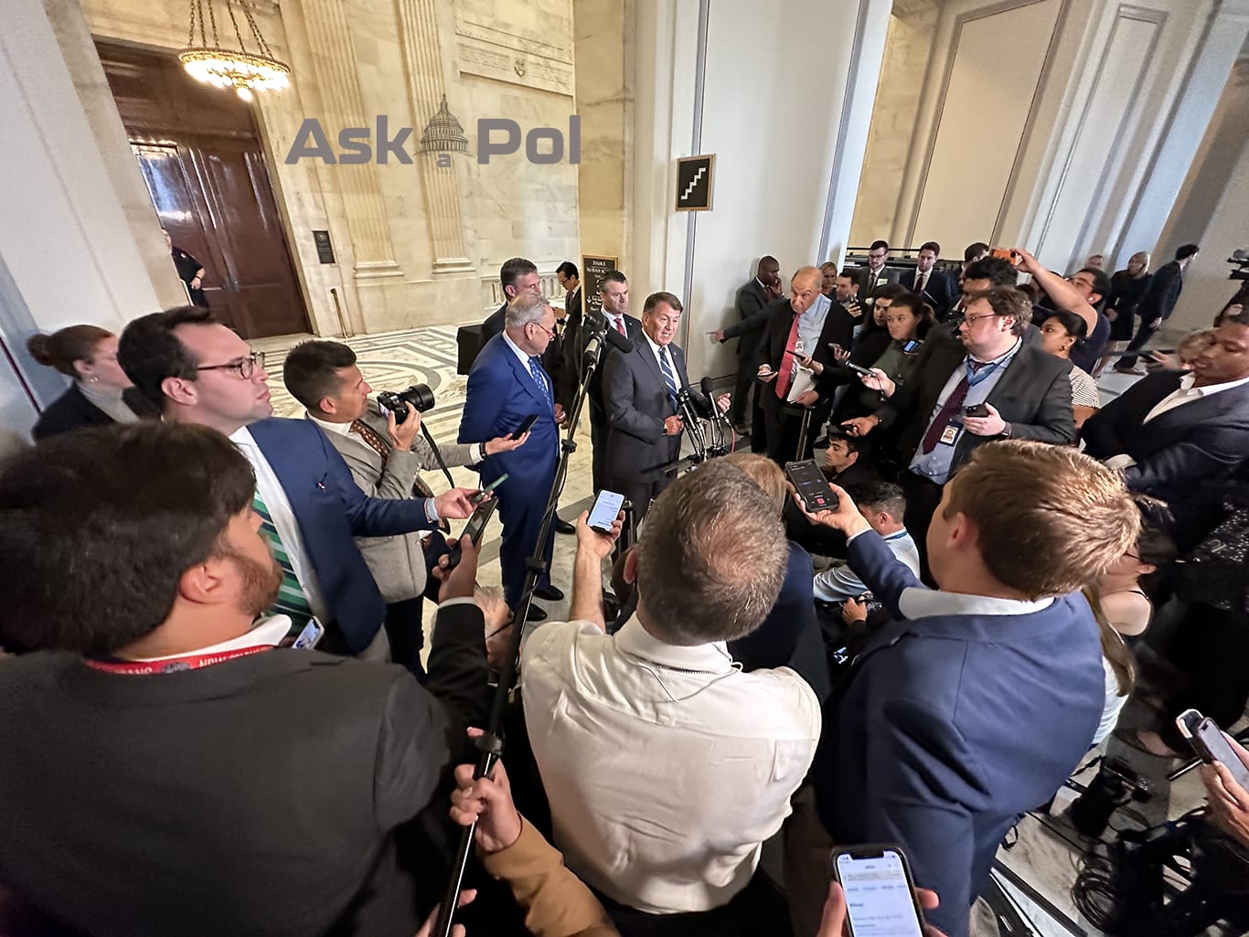 Dozens of reporters encircle four white male politicians in suits as cameras click and roll 