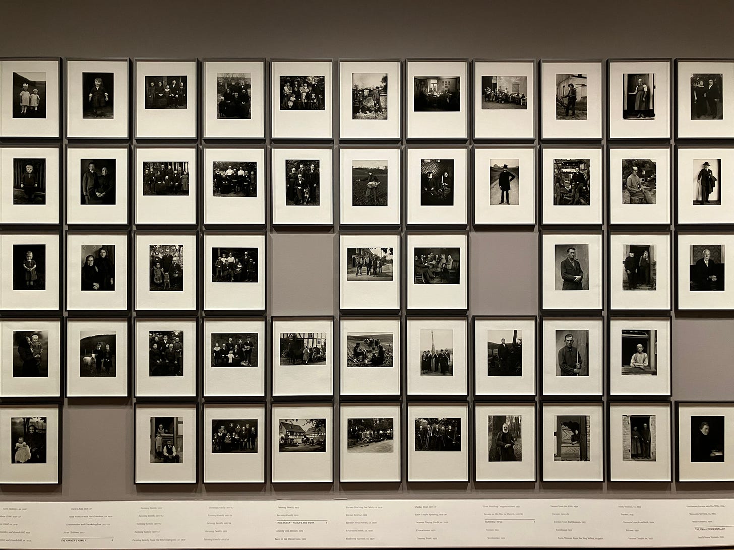 a gray wall with rows of black and white photographs hanging in a grid with a few blank spaces a gray wall with rows of black and white photographs hanging in a grid with a few blank spaces