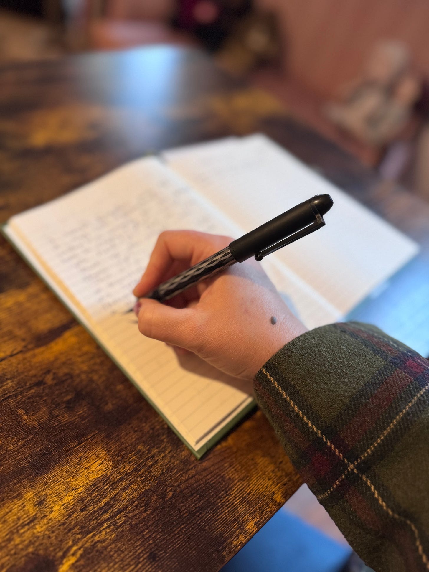 Amber writes on a piece of paper on her desk. The photo is taken from an angle, so you only see her hand holding the pen and writing and not the rest of her body or face.