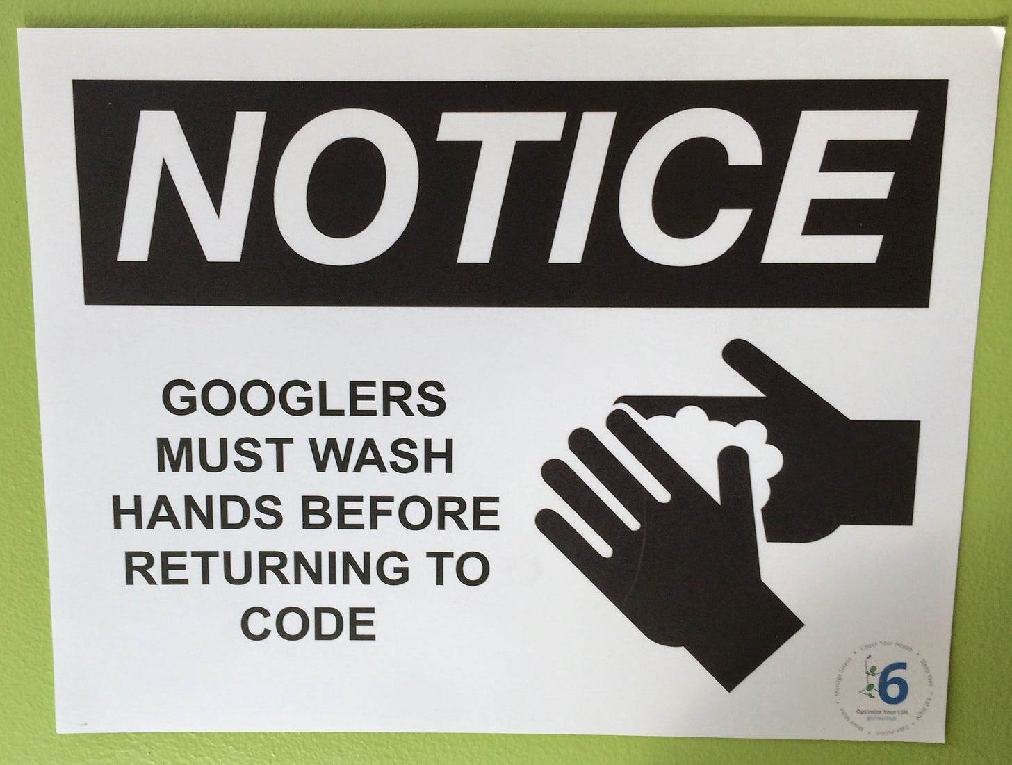 A sign reading "Notice: Googlers must wash hands before returning to code." There are two hands with soap on them.