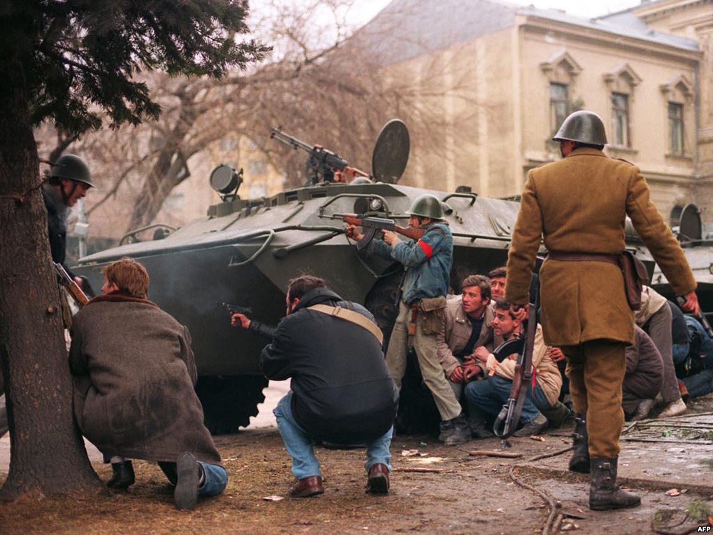 Civilian fighters and a Romanian soldier engaging in gunfire behind an APC during the Anti-Ceausescu uprising in Romania, 1989.