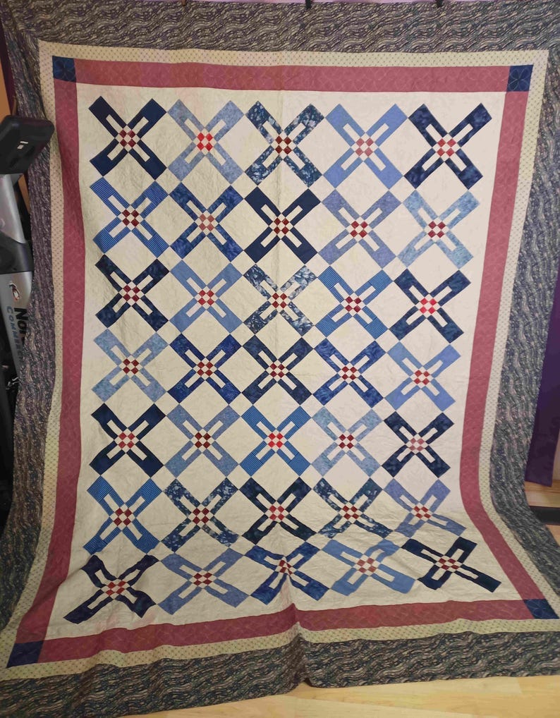 May include: A quilt with a patchwork design featuring blue, red, and white squares arranged in a grid pattern. The quilt is bordered with a red and white trim. May include: A quilt with a patchwork design featuring blue, red, and white squares arranged in a grid pattern. The quilt is bordered with a red and white trim.