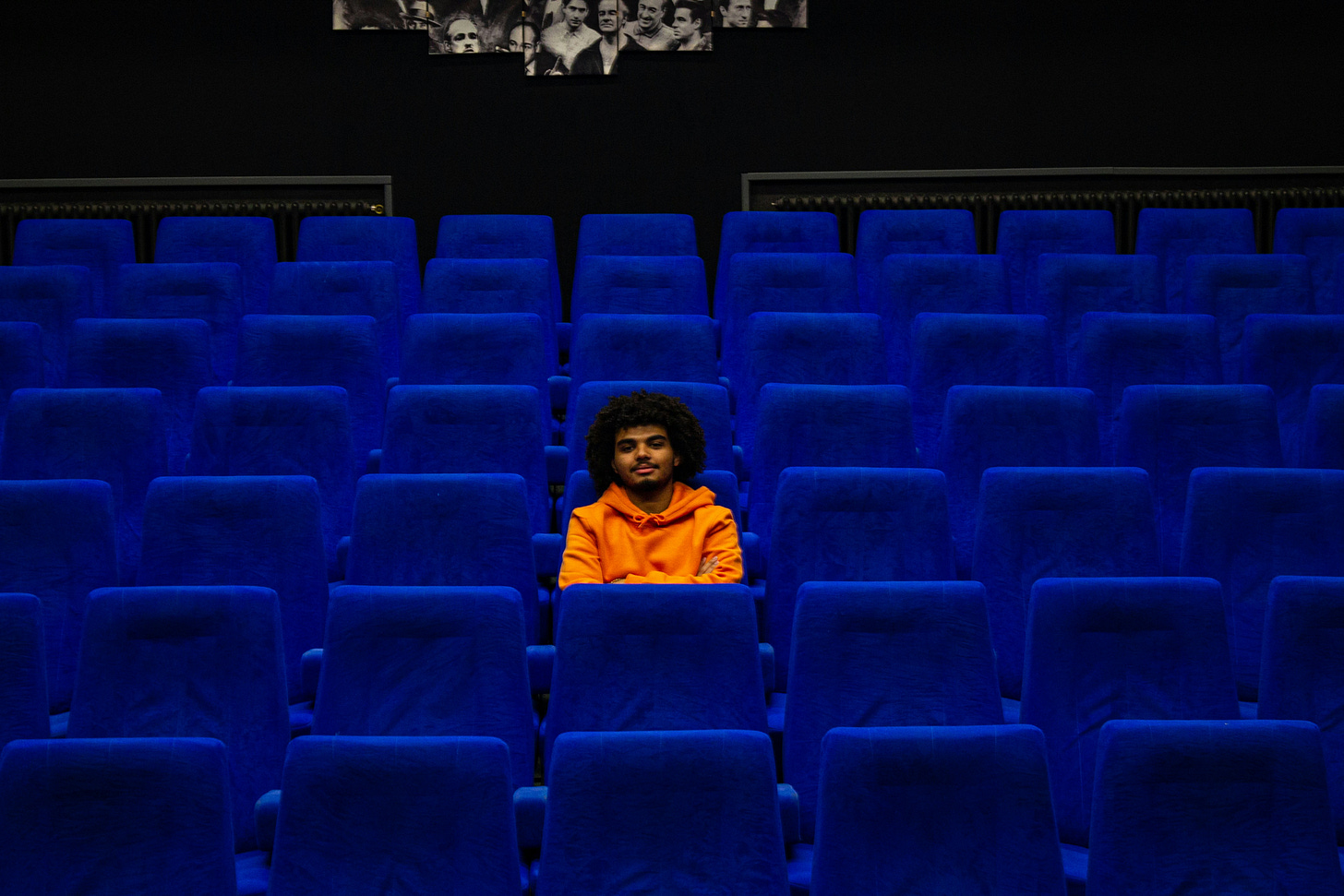 Audience seating, empty other than a single occupant who looks at us from his chair