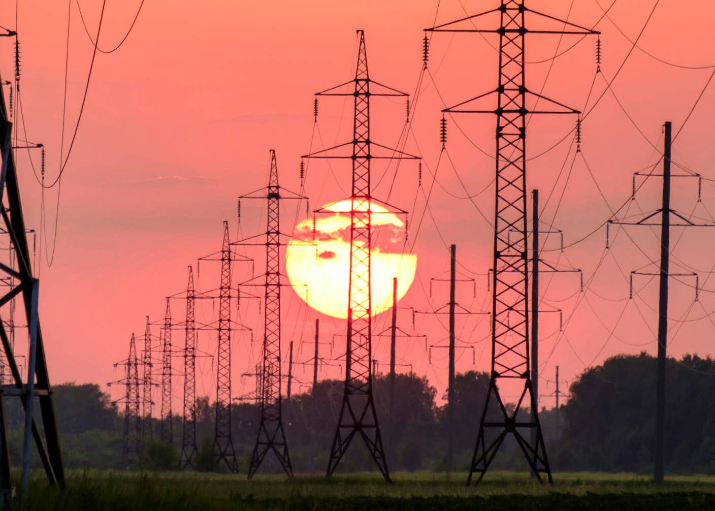 The sun and a red sky behind power lines marching into the distance The sun and a red sky behind power lines marching into the distance