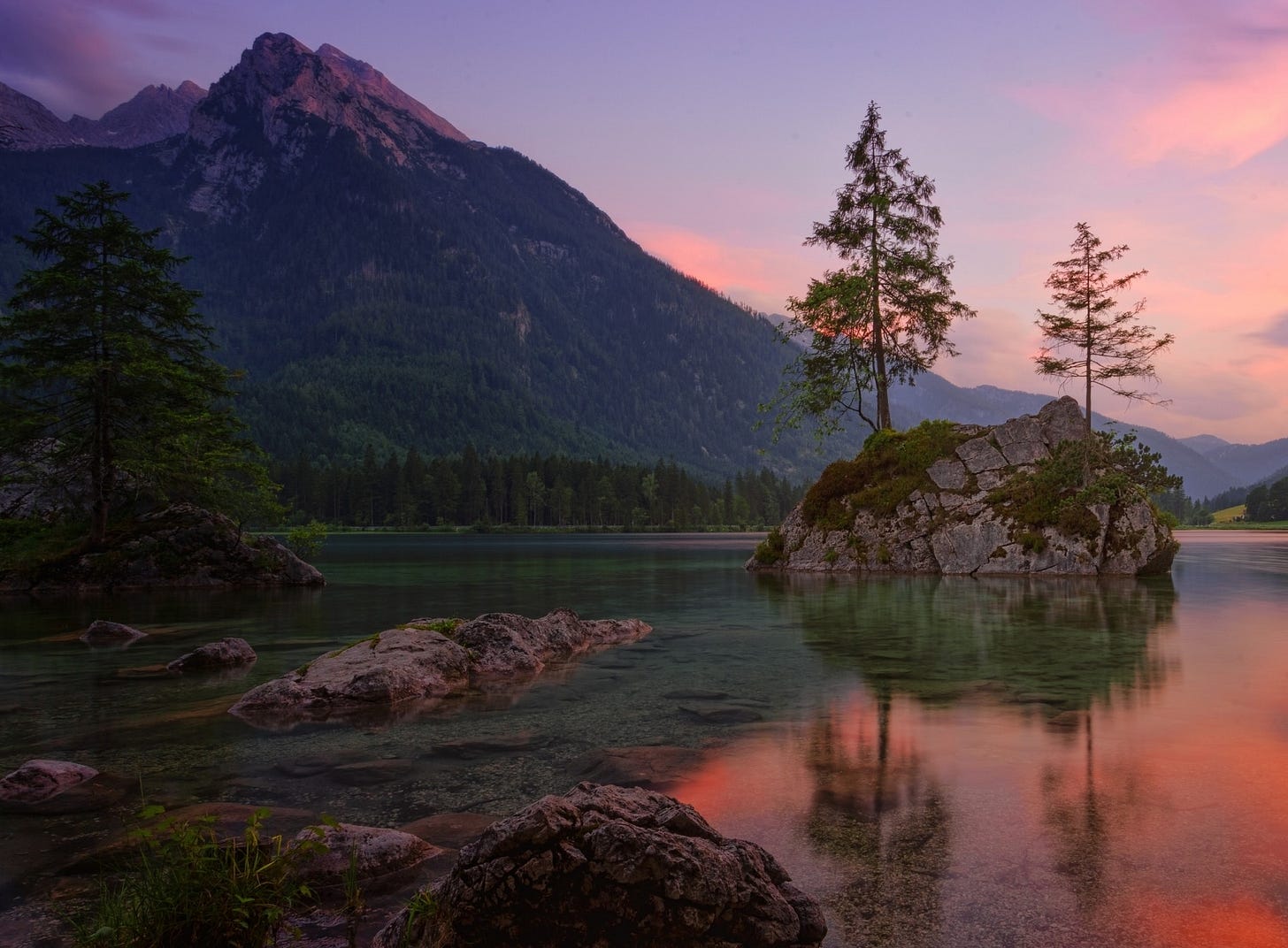 Two evergreen trees grow on a boulder in a mountain lake.