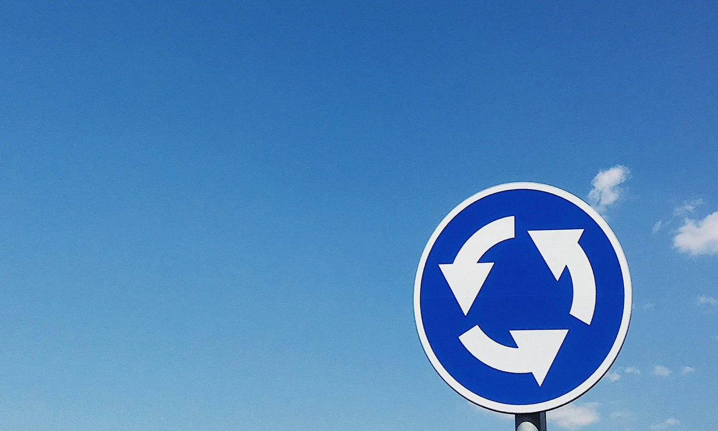 A roundabout traffic sign stands against a clear blue sky
