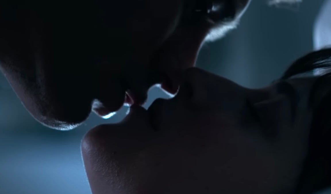 Intimate close-up of passionate kissing in dim light, building forbidden tension