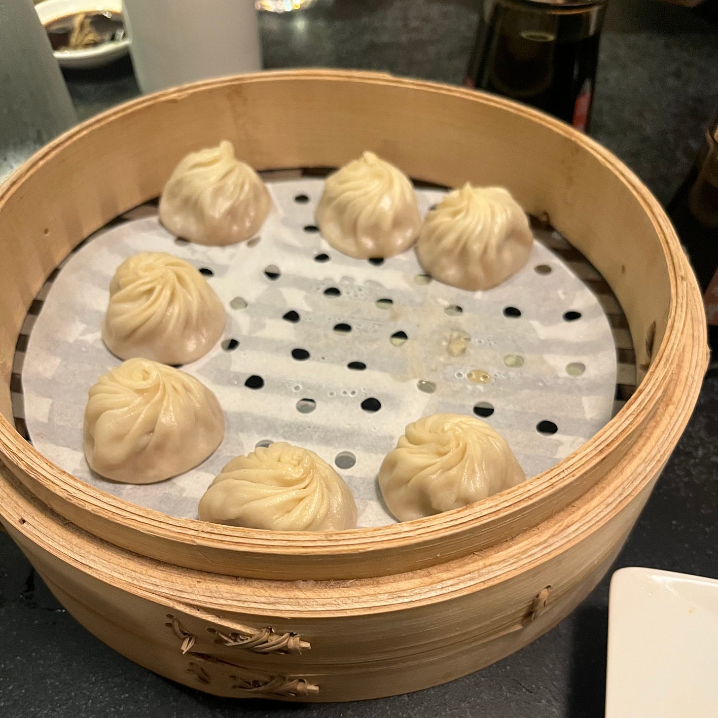 7 round dumplings with twisted skin, inside a round bamboo steamer