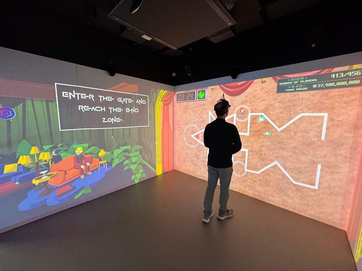A person stands in a room with projections on three walls, facing forward towards a maze-style display