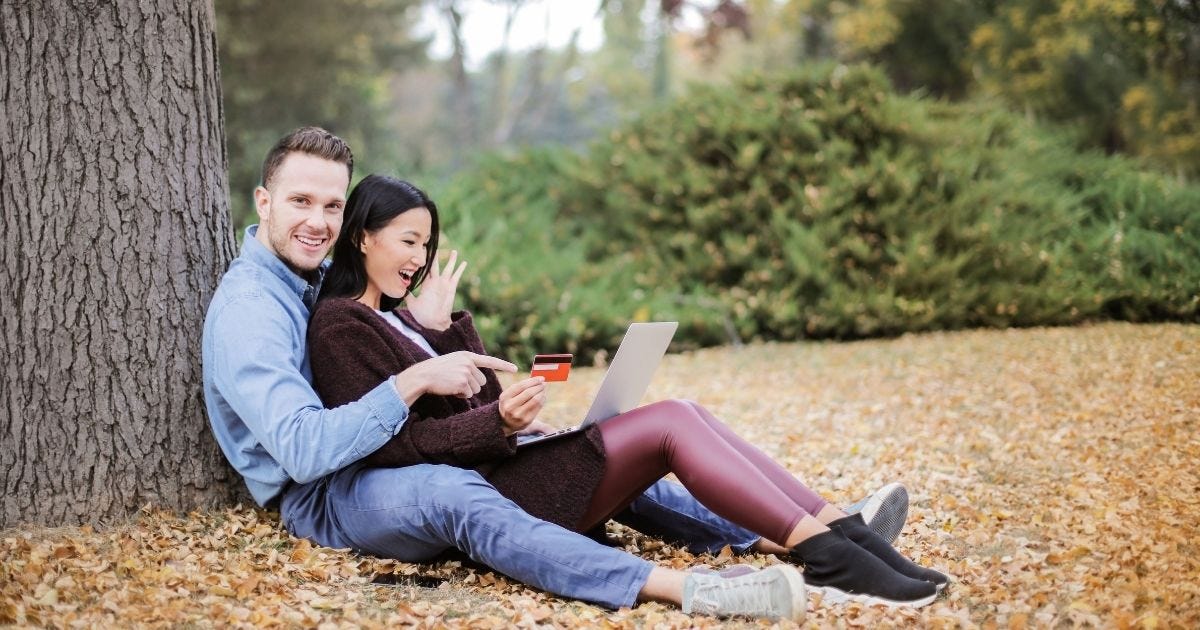 A couple using a laptop and credit card outdoors during fall A couple using a laptop and credit card outdoors during fall