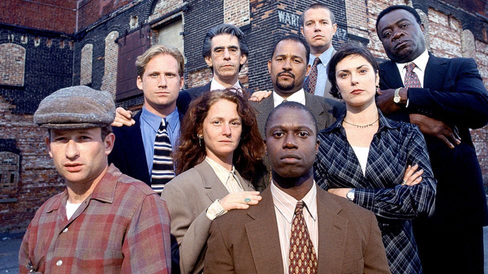 This image shows an official publicity photo of Homicide: Life on the Street’s Season 5 principal cast members. Front Row (left to right): Max Perlich (as J.H. Brodie) and Andre Braugher (as Detective Frank Pembleton). Second Row (left to right): Melissa Leo (as Det. Kay Howard) and Michelle Forbes (as Dr. Julianna Cox). Third Row (left to right): Reed Diamond (as Det. Mike Kellerman), Richard Belzer (as Det. John Munch), Clark Johnson (as Det. Meldrick Lewis) and Yaphet Kotto (as Lieutenant Al “Gee” Giardello). Back Row: Kyle Secor (as Det. Tim Bayliss).