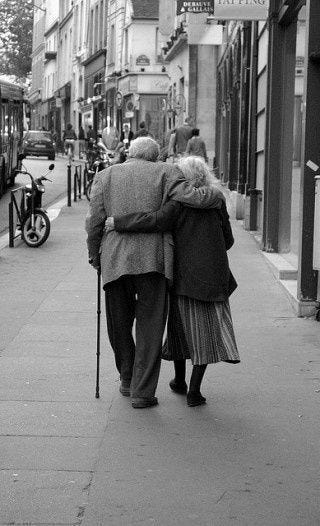 This may contain: an old man and woman walking down the street with their backs to each other,