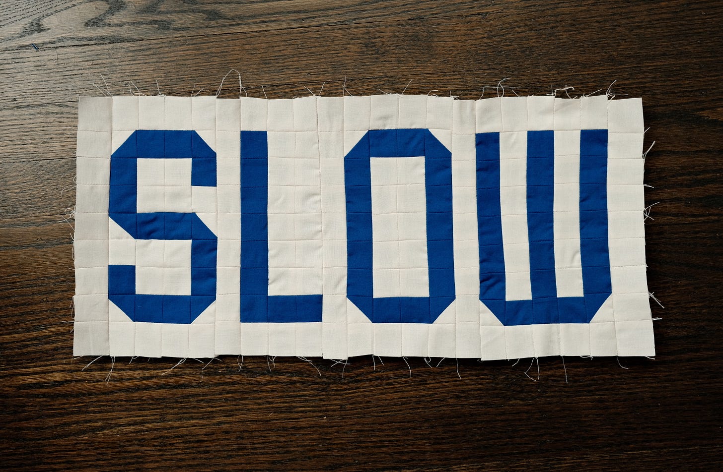 A work in progress of a quilted artwork, made of blue and white squares where the blue spells out the word "SLOW"