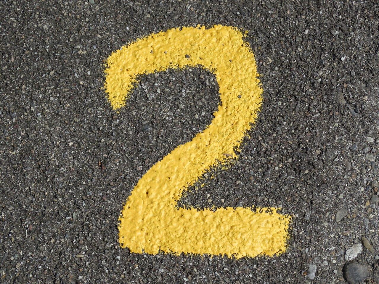 A number 2, spray painted in yellow on tarmac A number 2, spray painted in yellow on tarmac
