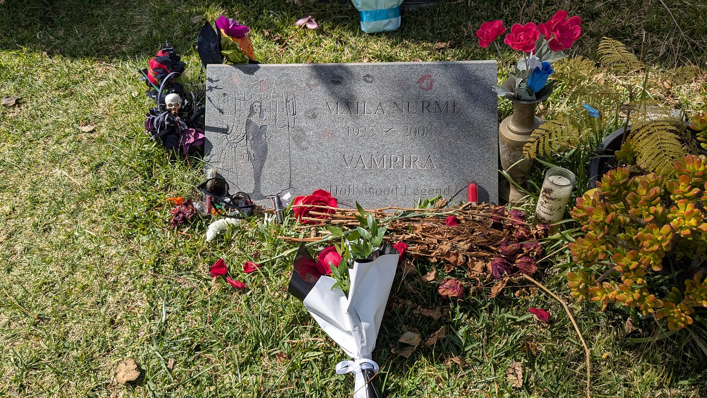 A granite headstone surrounded by flowers and macabre trinkets to commemorate Maila Nurmi otherwise known as Vampira