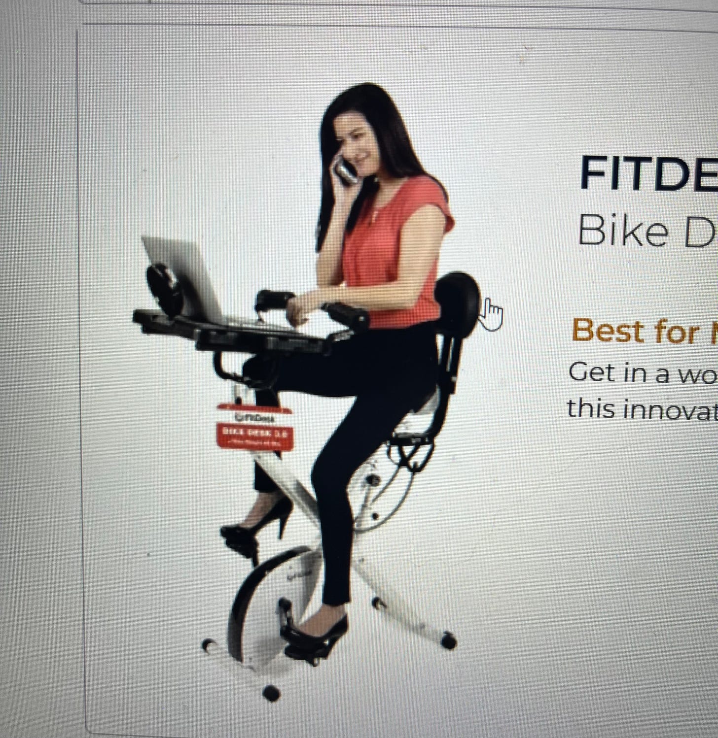 Dark haired woman wearing black heels, black pants, a red short-sleeved blouse sitting on a compact stationary bike with a desk attachment and laptop. Dark haired woman wearing black heels, black pants, a red short-sleeved blouse sitting on a compact stationary bike with a desk attachment and laptop.