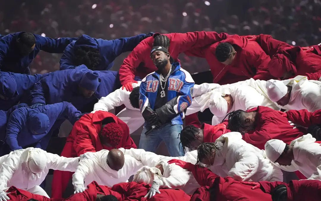 Kendrick Lamar stands amid men wearing red, white, and blue clothing during the Super Bowl Halftime Performance in 2025