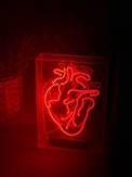 A red neon outline of a human heart in a glass frame.