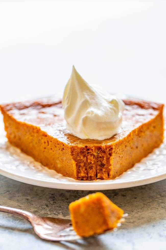 slice of crustless pumpkin pie topped with whipped cream on a white plate. a fork rests in the foreground. slice of crustless pumpkin pie topped with whipped cream on a white plate. a fork rests in the foreground.