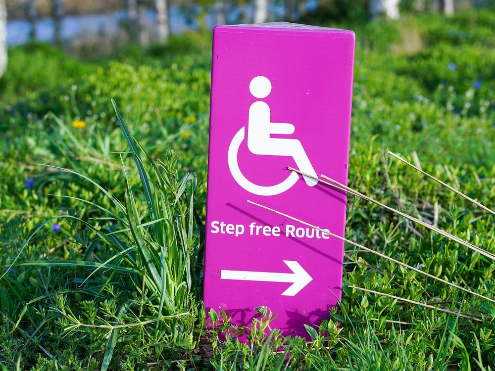 A pink lawn marker pointing wheelchair users to an accessible path.