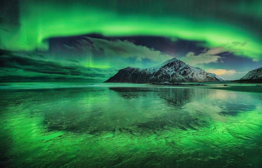 A wide view of a bright-green aurora above a snow-covered mountain, appearing like a shimmering curtain in the sky. A wide view of a bright-green aurora above a snow-covered mountain, appearing like a shimmering curtain in the sky.