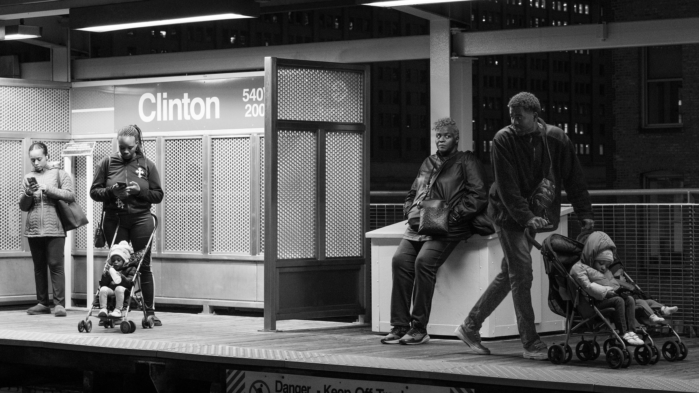 Black and white photo of people interacting and not interacting on "L" platform.