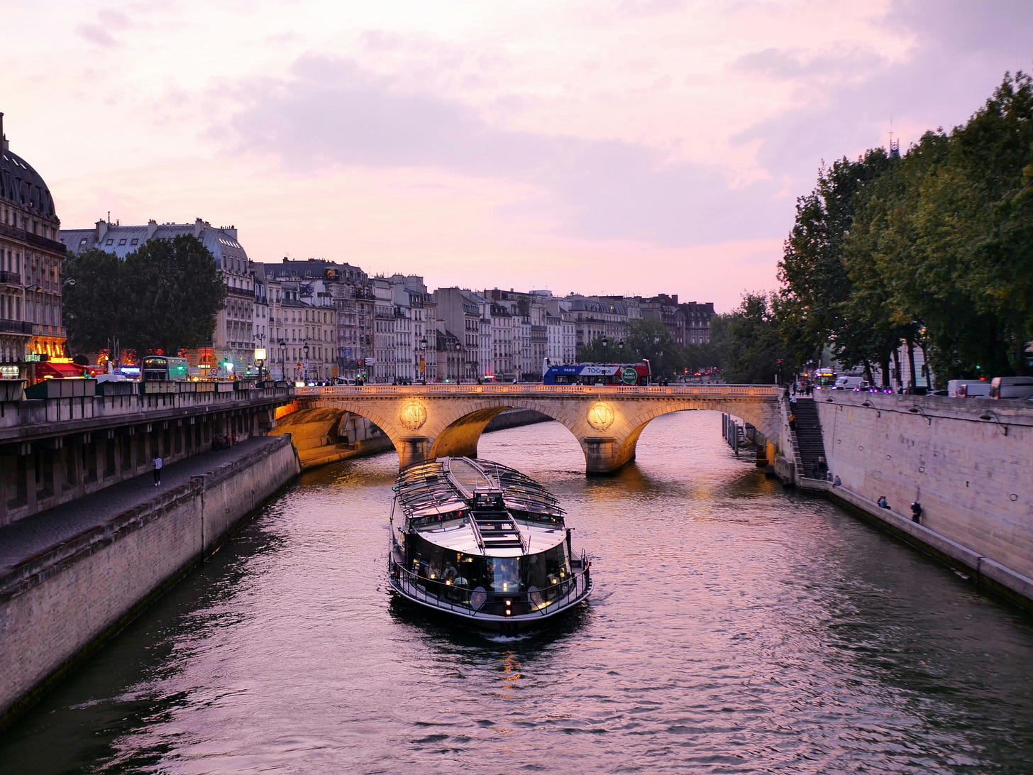 The Seine Rivier in Paris, flanked by the two Quays and featuring a sightseeing boat at sunset