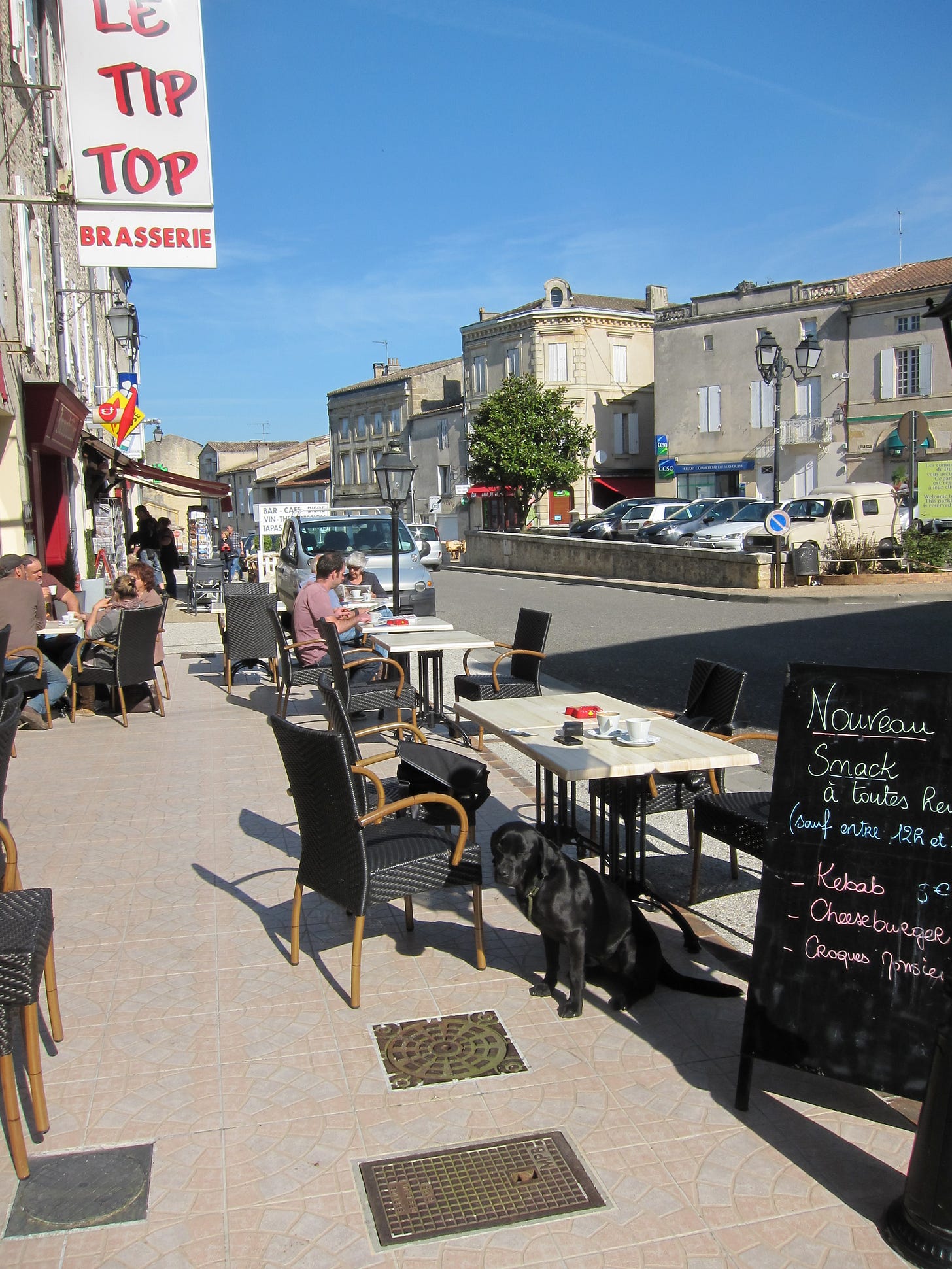 A black labrador sat near a table in an outdoor seating area of a brasserie
