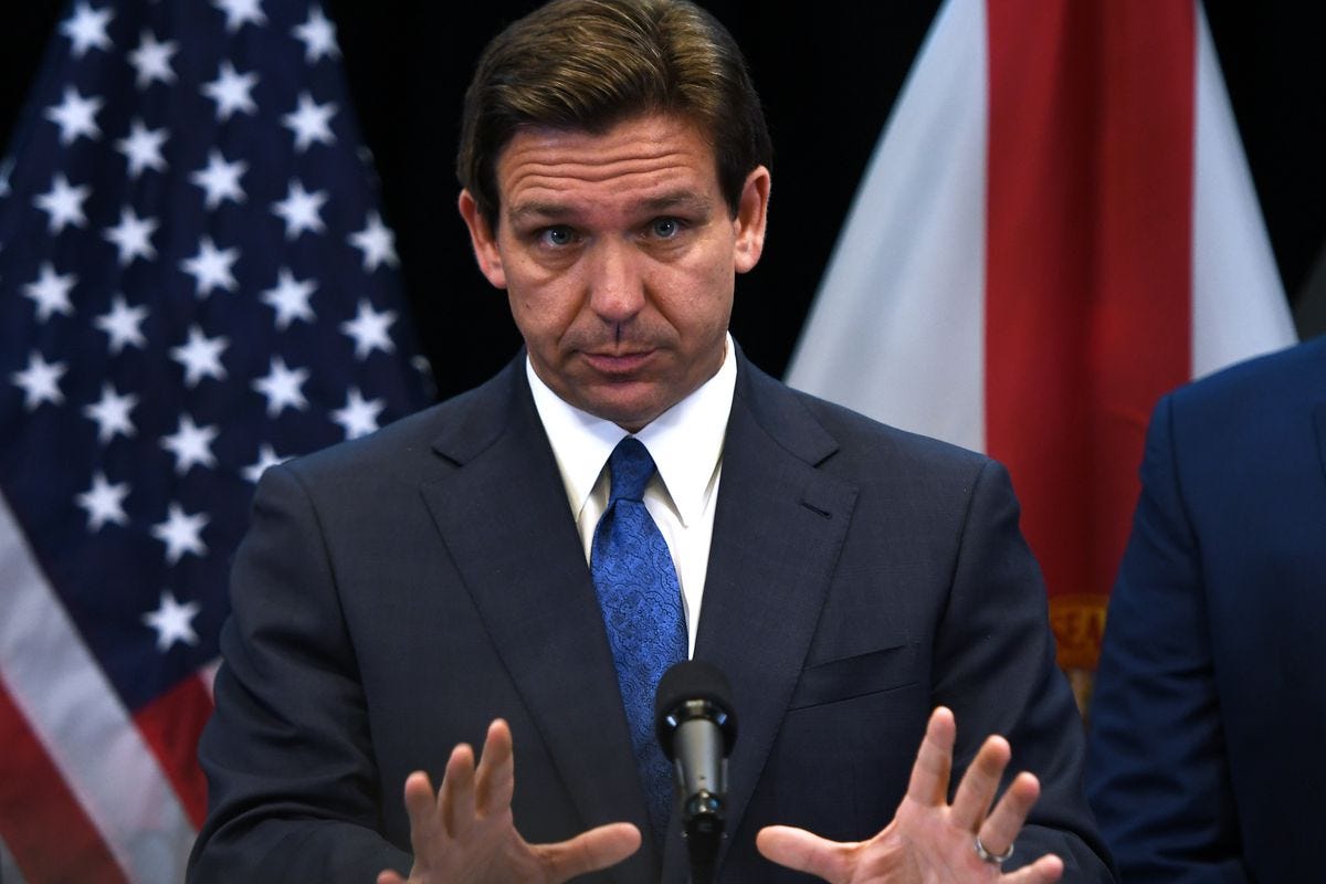DeSantis gestures with both hands while holding a press conference, standing in front of a US flag. DeSantis gestures with both hands while holding a press conference, standing in front of a US flag.